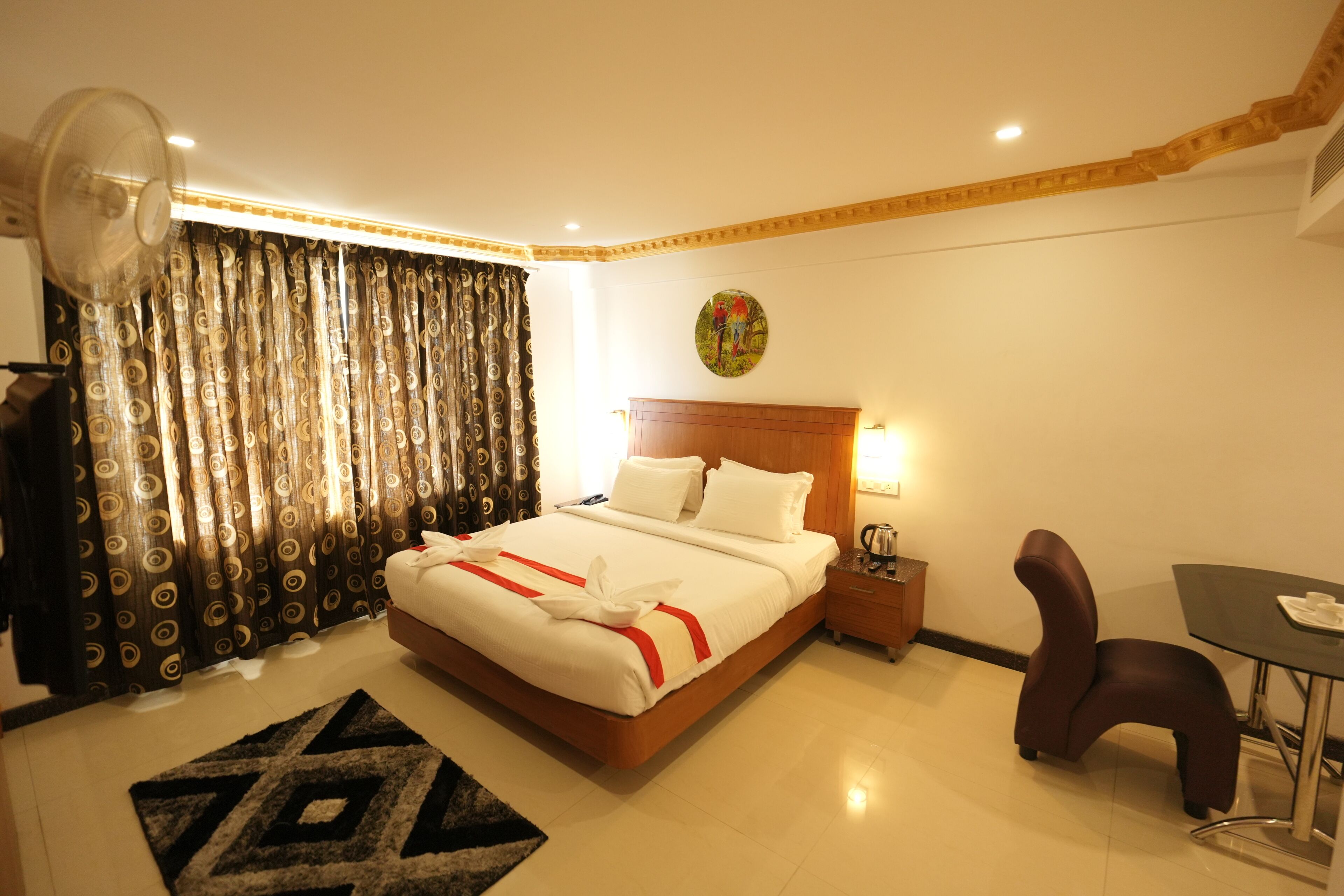 A hotel room with a bed, a desk, a chair, a fan, and curtains.