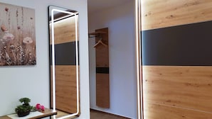 Moderni huone, jossa on suuri peili, puupaneloidut seinät, pieni viherkasvi ja puinen naulakko.