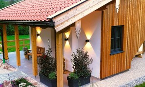 A wooden building with a red-tiled roof, a wooden porch, and two potted plants. - 80-square-meter chalet for 1–2 people, with a living room, kitchen, bedroom, bathroom, and separate toilet (Marquartstein)