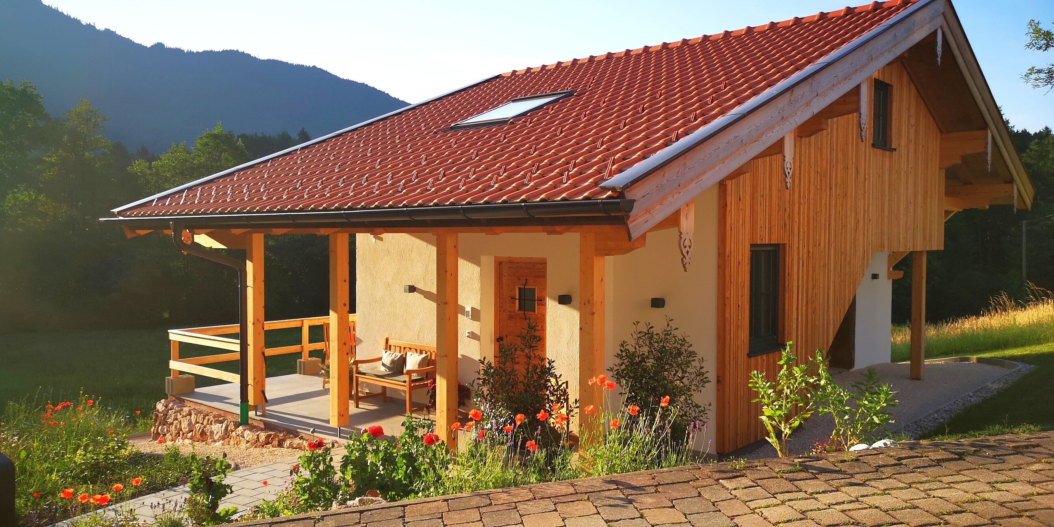 Ein Holzhaus mit rotem Ziegeldach, einer Veranda und einem Garten mit roten Blumen.