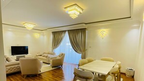 A modern living room with a wooden floor, a sofa, a TV, a dining table with chairs, and a chandelier. - Abat property (Addis Ababa)