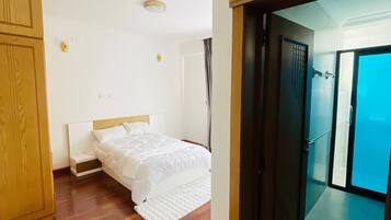 Camera d'albergo con pavimento in legno, un letto con biancheria bianca, un armadio in legno e una porta che dà su un balcone.