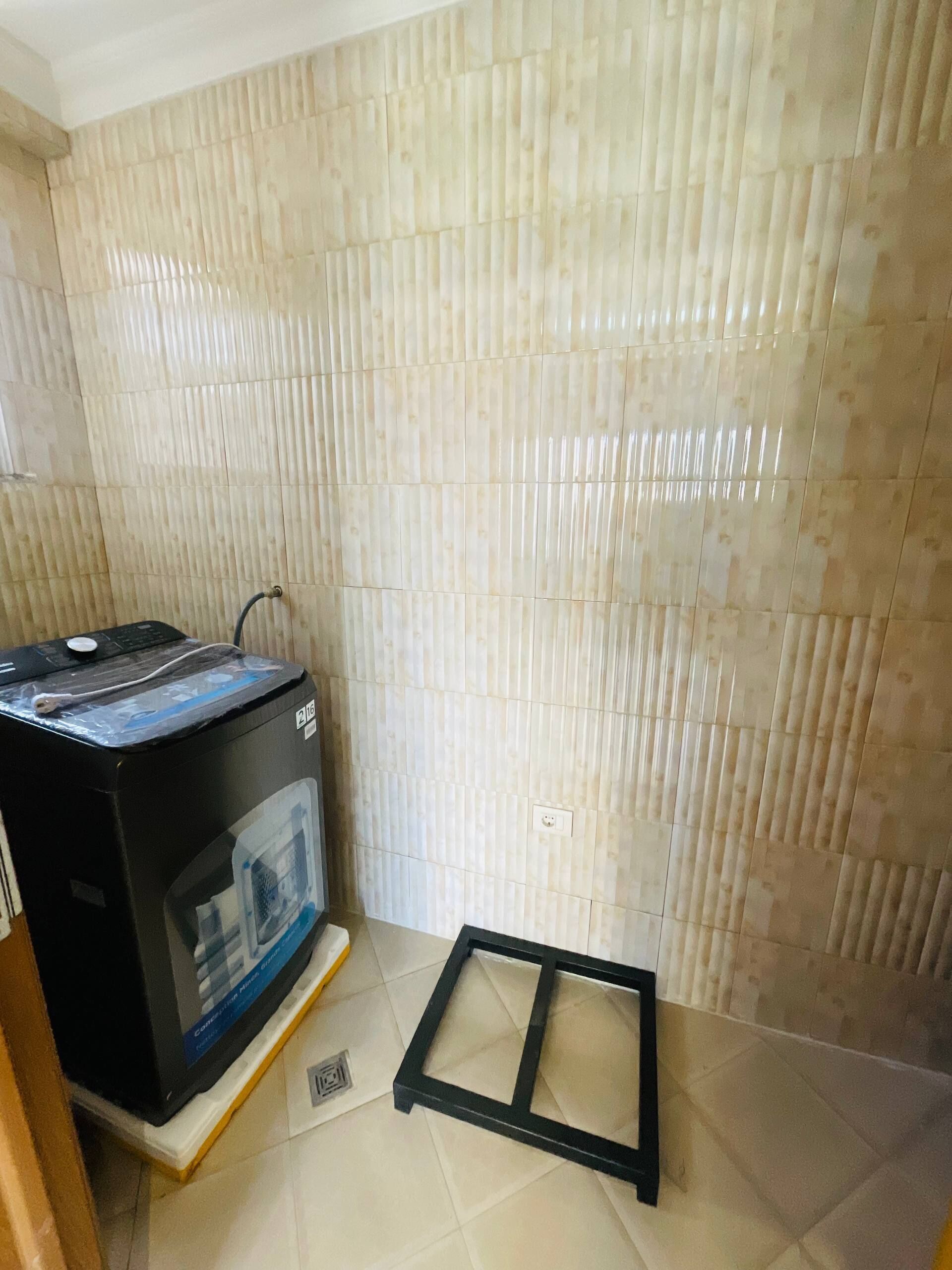 Una habitación con pared de azulejos, un electrodoméstico negro sobre un pedestal y un marco negro en el suelo.