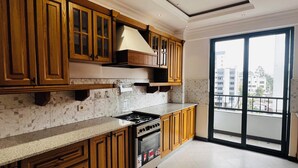 A kitchen with wooden cabinets, a stove, and a large window. - Abat property (Addis Ababa)