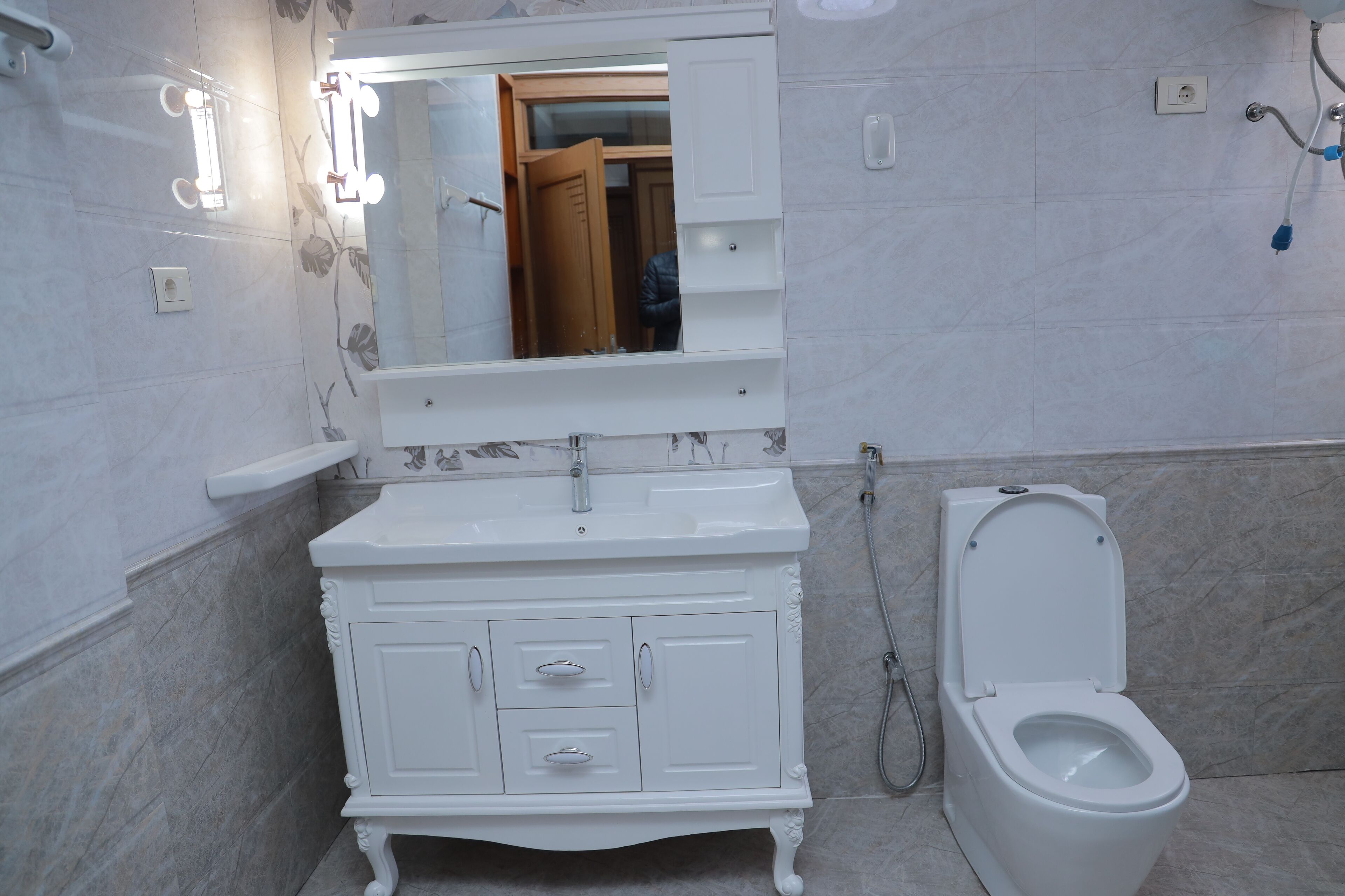 Un baño con tocador blanco, un espejo con iluminación, inodoro y zona de ducha.