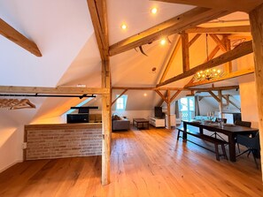 Ein geräumiger Lofts mit freiliegenden Holzbalken, einem Schlafbett im erhöhten Bereich, einer Essecke mit einer Chandelierleuchtre und einer Ziegelwand.