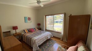 Een slaapkamer met een bed, een bureau, een stoel, een raam met uitzicht en een plafondventilator.