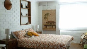 Un dormitorio con una colcha estampada, una mesita de noche con lámpara, una estantería con adornos y un cuadro en la pared.