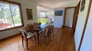 Een eethoek met een houten tafel en stoelen, een raam met uitzicht op bomen en een keuken op de achtergrond.