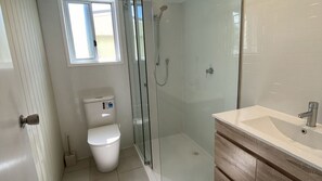 Un baño moderno con cabina de ducha de vidrio, inodoro y tocador con lavamanos.