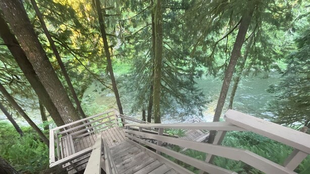 A wooden staircase leading down to a forested area with a river. - Forks Riverside Serenity (Forks)