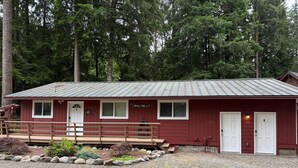 A red building with two doors, a wooden deck, and a gravel driveway. - Forks Riverside Serenity (Forks)