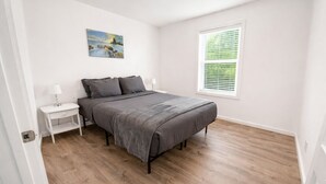 Ein Schlafzimmer mit einem Bett, einem Nachttisch, einem Gemälde und einem Fenster mit Jalousien.