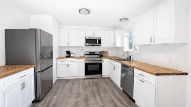 Eine moderne Küche mit weißen Schränken, Edelstahlgeräten und einer Holzausziehtafel.