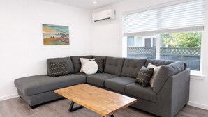 Ein modernes Wohnzimmer mit einem grauen Ecksofa, einem Holztisch und gemusterten Kissen.
