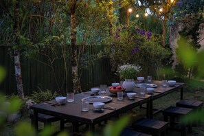 An outdoor dining area with a long table set for a meal, surrounded by greenery and a wooden fence. - The New House (Xuan Huong - Da Lat)