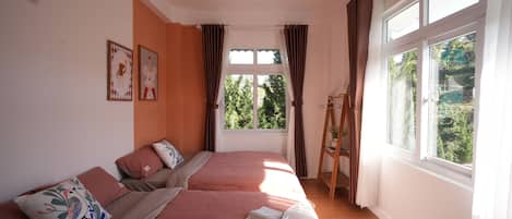 Une chambre avec deux lits, une fenêtre avec des rideaux, une échelle et un bol de pommes posé sur l’un des lits.