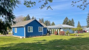 A blue house with a sloped roof, surrounded by a well-maintained lawn and trees. - Bogachiel Den – Comfortable Forks Getaway (Forks)