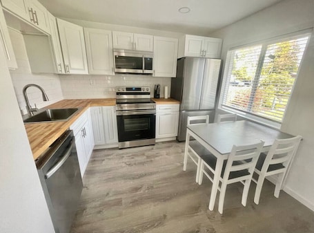 A modern kitchen with white cabinets, stainless steel appliances, a wooden countertop, and a dining area with a table and chairs.