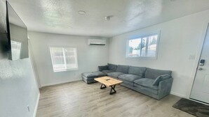 A spacious living room with a grey sectional sofa, a wooden coffee table, and a large window providing natural light. - Bogachiel Den – Comfortable Forks Getaway (Forks)