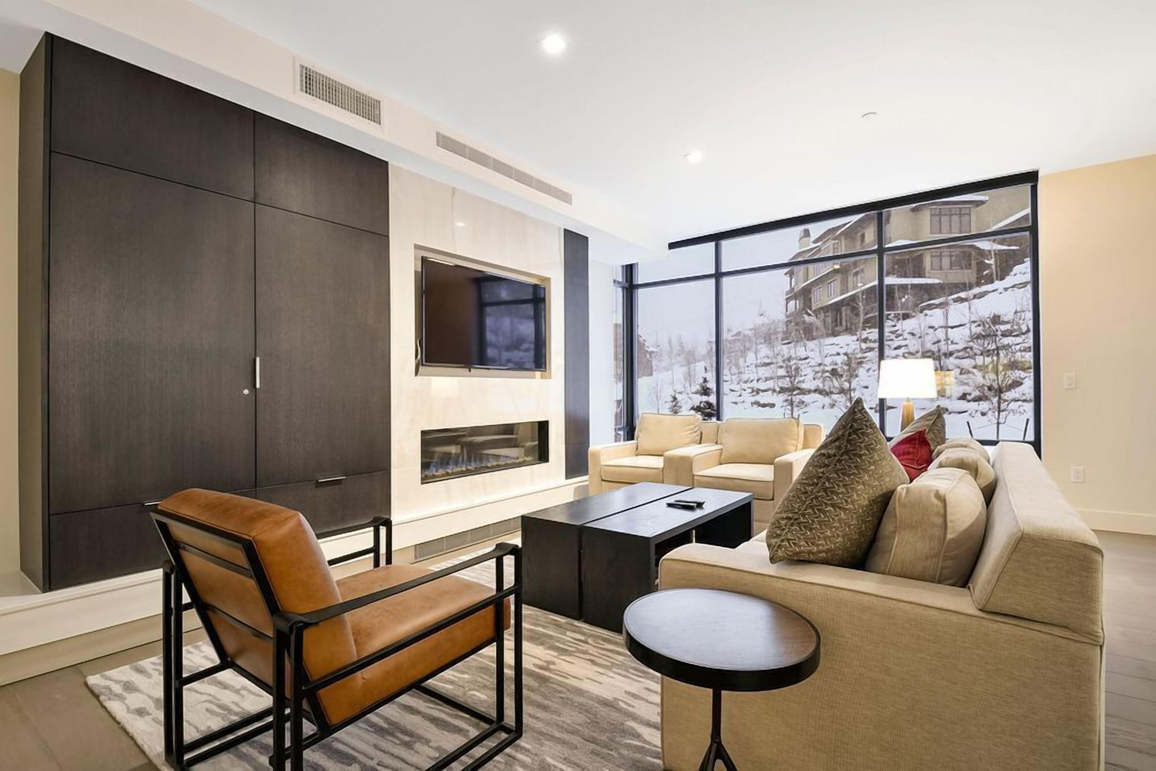 A modern living room with a fireplace, a large window with a snowy view, and a sofa set.