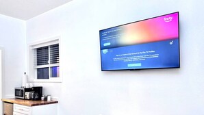 Moderni keittiö, jossa on mikroaaltouuni, kahvinkeitin ja kaappeja. Seinälle on asennettu taulutelevisio, jossa näkyy Amazon Fire TV -profiileja koskeva ilmoitus.