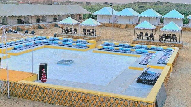 Un resort en el desierto con varias tiendas de campaña y una amplia piscina exterior con tumbonas.