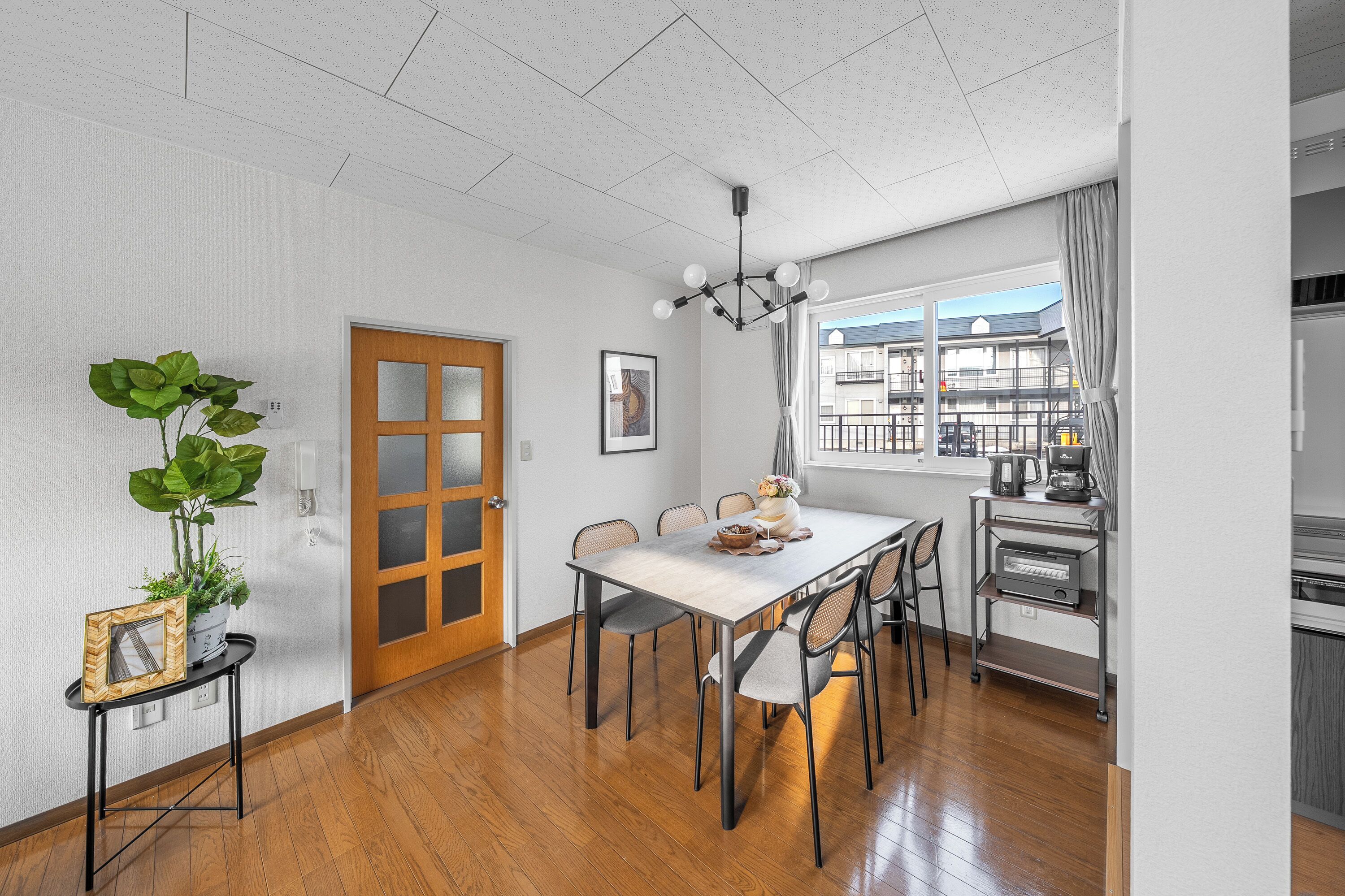 A modern kitchen with a dining area, featuring a wooden floor, a white table, and a chandelier.