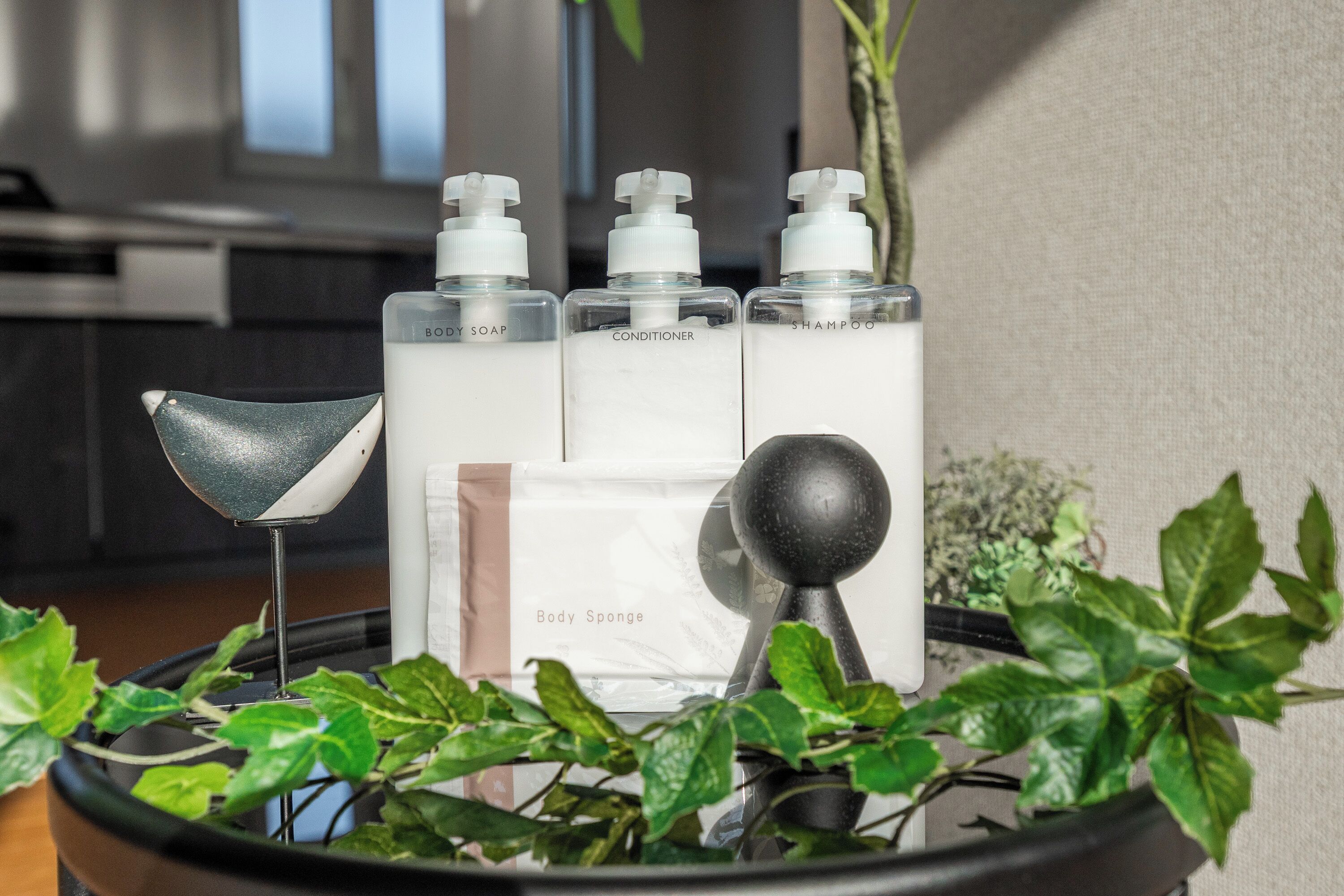 Une salle de bain avec un plateau noir contenant des articles de toilette, une éponge pour le corps et un objet décoratif noir.