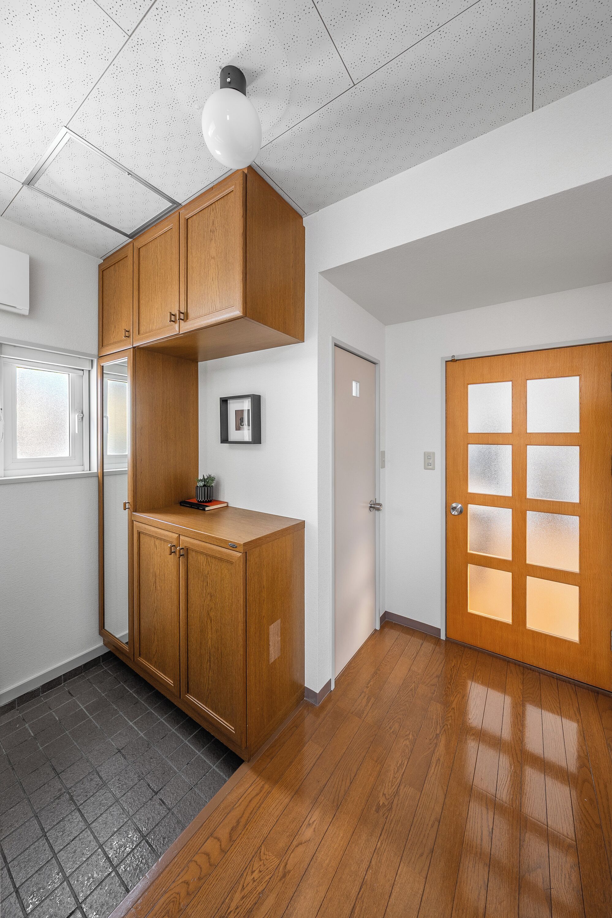 Ein Zimmer mit Holzausstattung, einem gerahmten Bild, einer Tür mit Milchglasfenstern und einem Fenster.