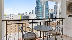 Un balcon avec une table et deux chaises, donnant sur un paysage urbain avec de hauts immeubles.