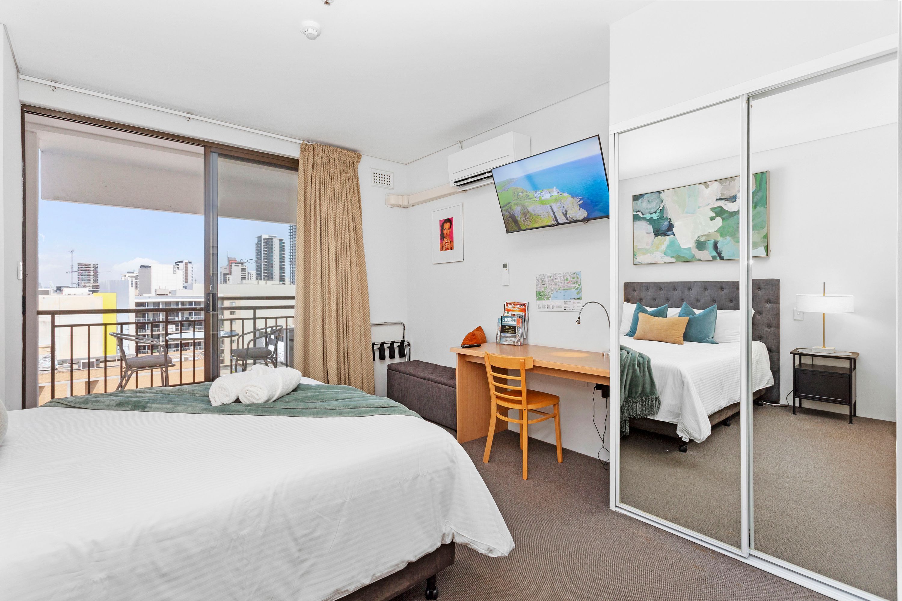 A hotel room with a bed, a desk, a chair, a TV, and a balcony with city views.
