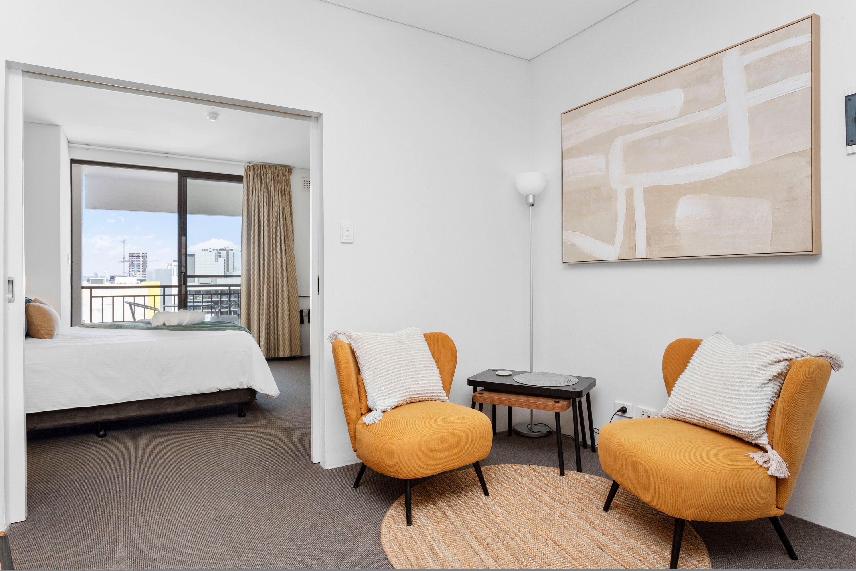 A hotel room with a bed, two armchairs, a small table, a rug, and a large abstract painting on the wall.