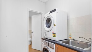 Une petite buanderie équipée d’un lave-linge à chargement frontal, d’un sèche-linge et d’un évier.