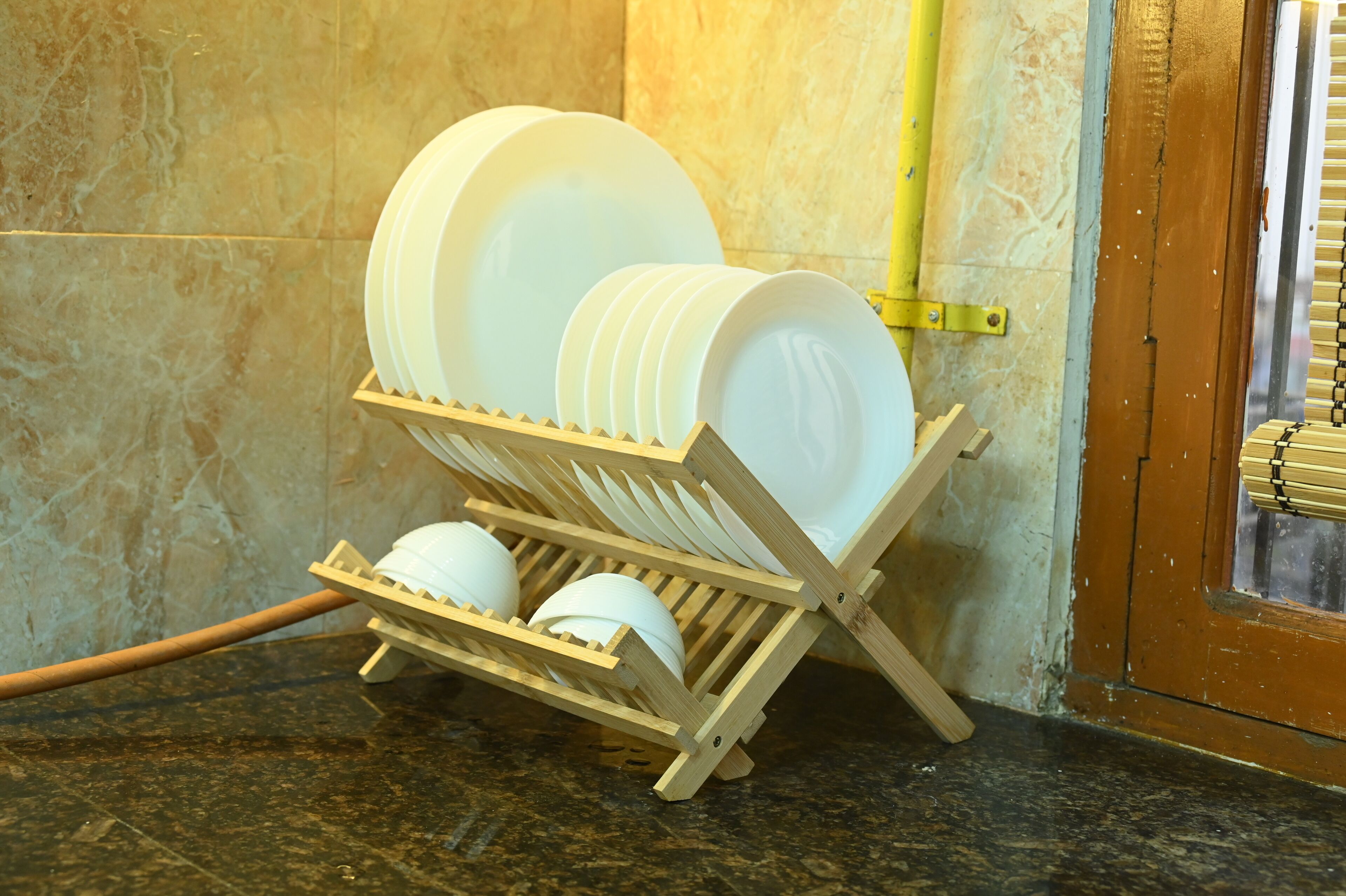 A wooden dish rack with white plates and bowls in a kitchen.