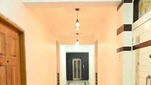 Un couloir avec une porte en bois sur la gauche, une porte en verre au fond, et un mur orné d’un panneau décoratif sur la droite.