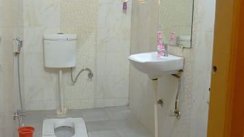 Un baño pequeño con inodoro, lavamanos, ducha y un cubo.