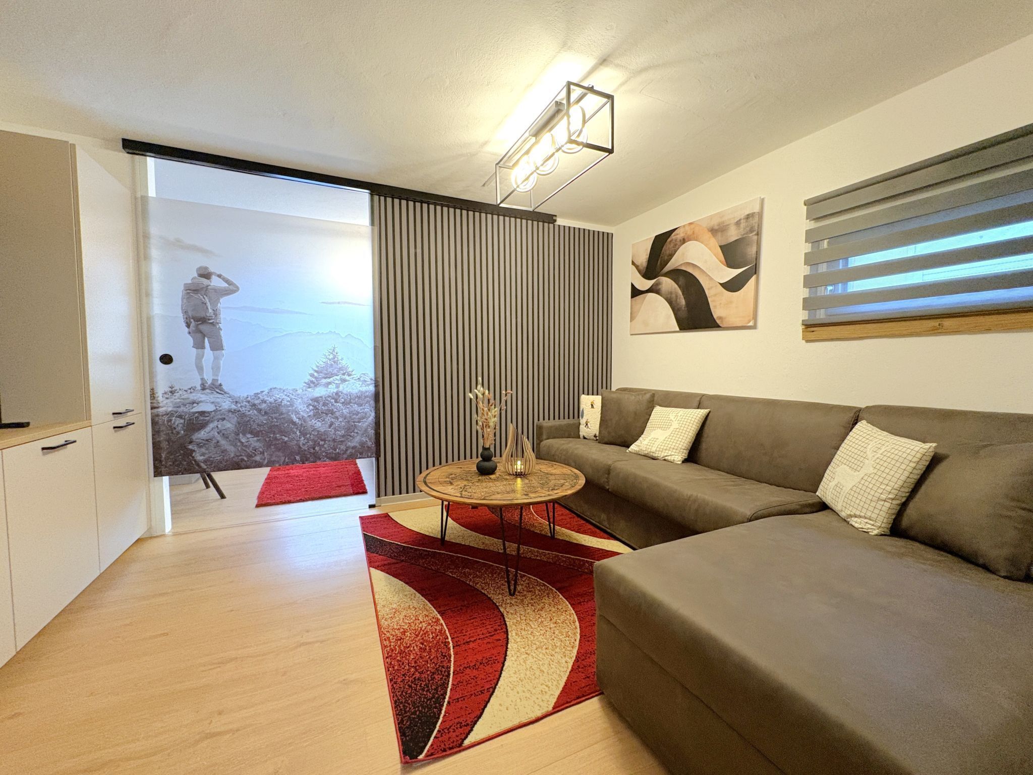 Una sala de estar moderna con sofá, una mesa de centro y un tapete rojo. Hay una puerta corredera que da a un balcón con vistas.