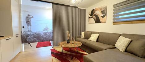 Una sala de estar moderna con sofá, una mesa de centro y un tapete rojo. Hay una puerta corredera que da a un balcón con vistas.