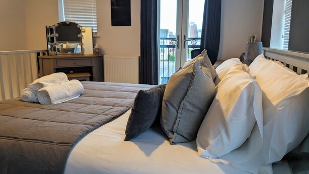 A neatly made bed with a quilted cover, pillows, and rolled towels. - Canal-side haven, short canal walk to city. Pet Friendly and parking! (Leeds)