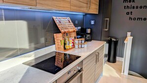 A modern kitchen with a built-in stove, a coffee machine, and a wicker basket containing kitchen essentials. - Canal-side haven, short canal walk to city. Pet Friendly and parking! (Leeds)