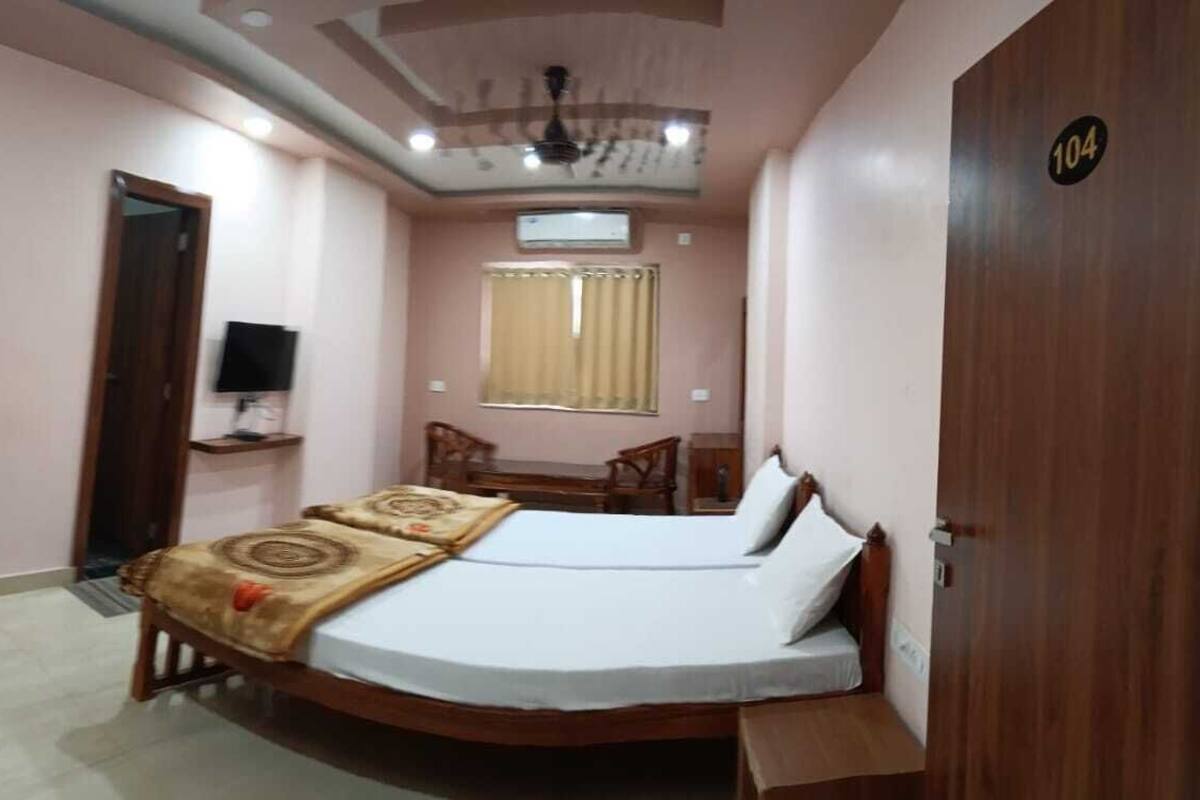 A compact bedroom with a single bed, a television on a stand, a small table, and a wardrobe.
