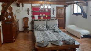 Une chambre traditionnelle avec un lit en bois, un banc avec des serviettes, une armoire en bois et un mur rouge agrémenté d’étagères.