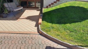 Un espace patio aménagé avec un fauteuil suspendu, des plantes en pot et un escalier en pierre menant à une porte.