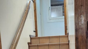 Un escalier recouvert de carreaux beiges et doté de rampes en bois, menant à une pièce avec une fenêtre et un ventilateur de plafond.