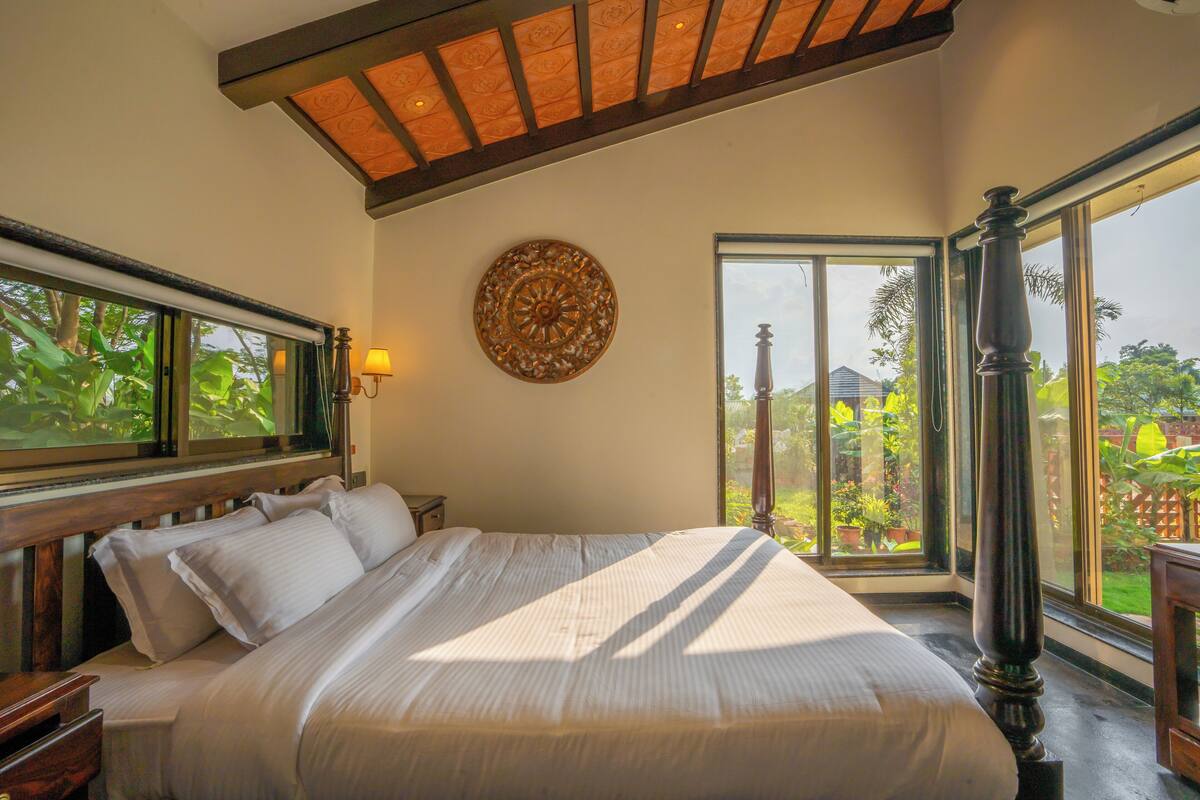 A bedroom with a large bed, a wooden headboard, a decorative wall hanging, and a view of the outdoors through a large window.
