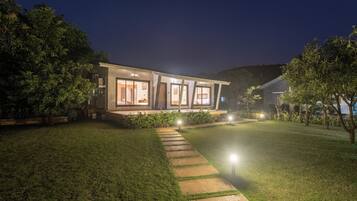 A modern house with a well-lit exterior, a stone pathway leading to the entrance, and a lush green lawn.