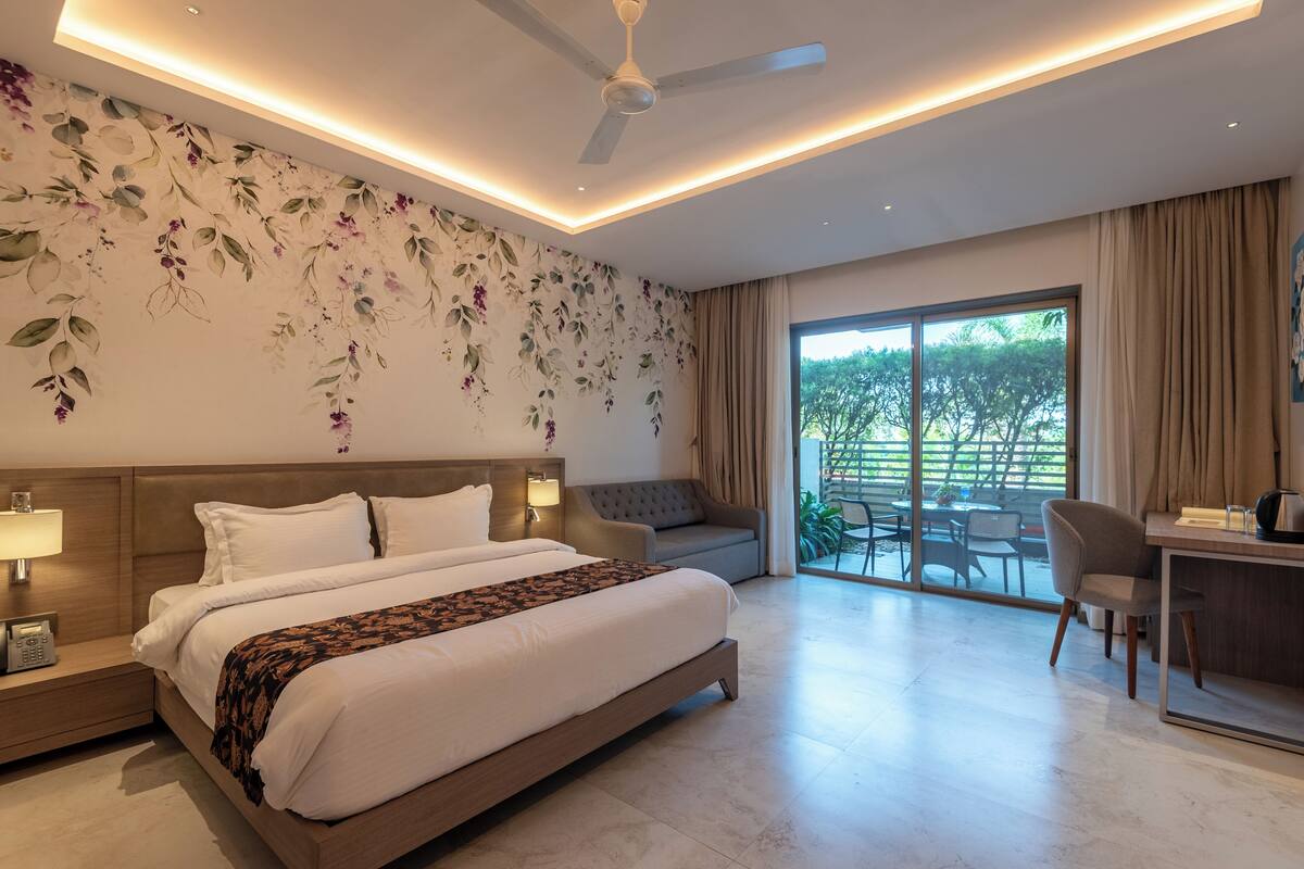 A modern hotel room with a large bed, a desk, and a balcony with a view.