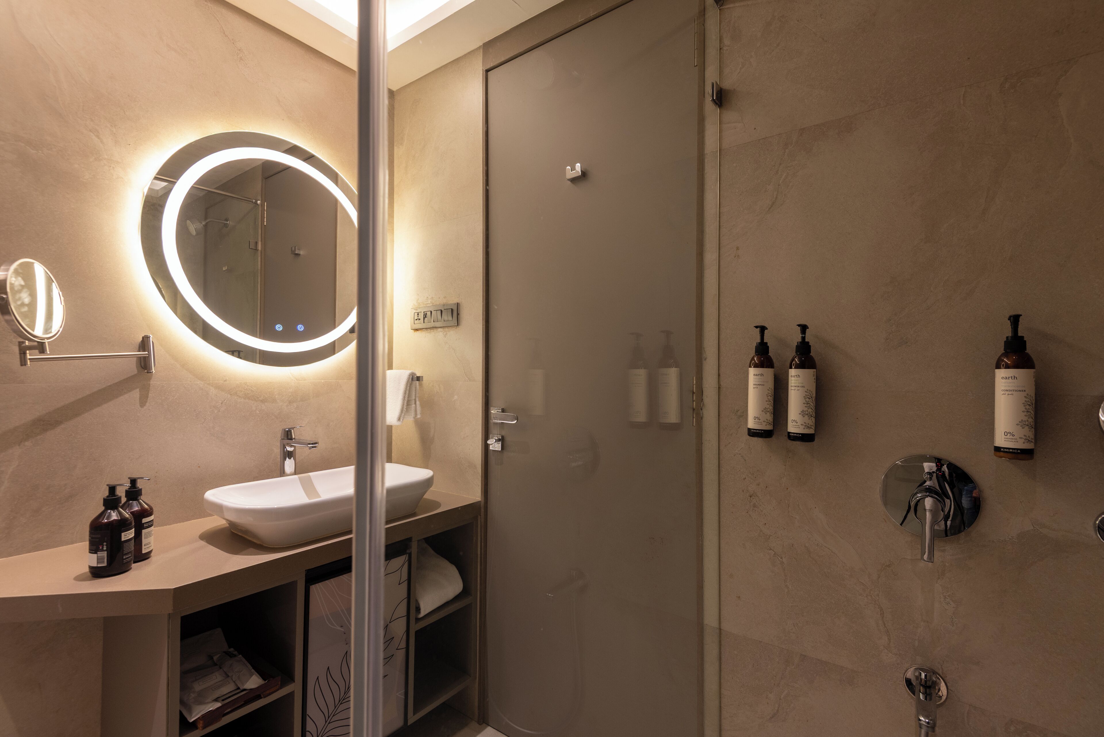 Un baño moderno con un espejo redondo, un lavamanos y una ducha con mampara de vidrio.