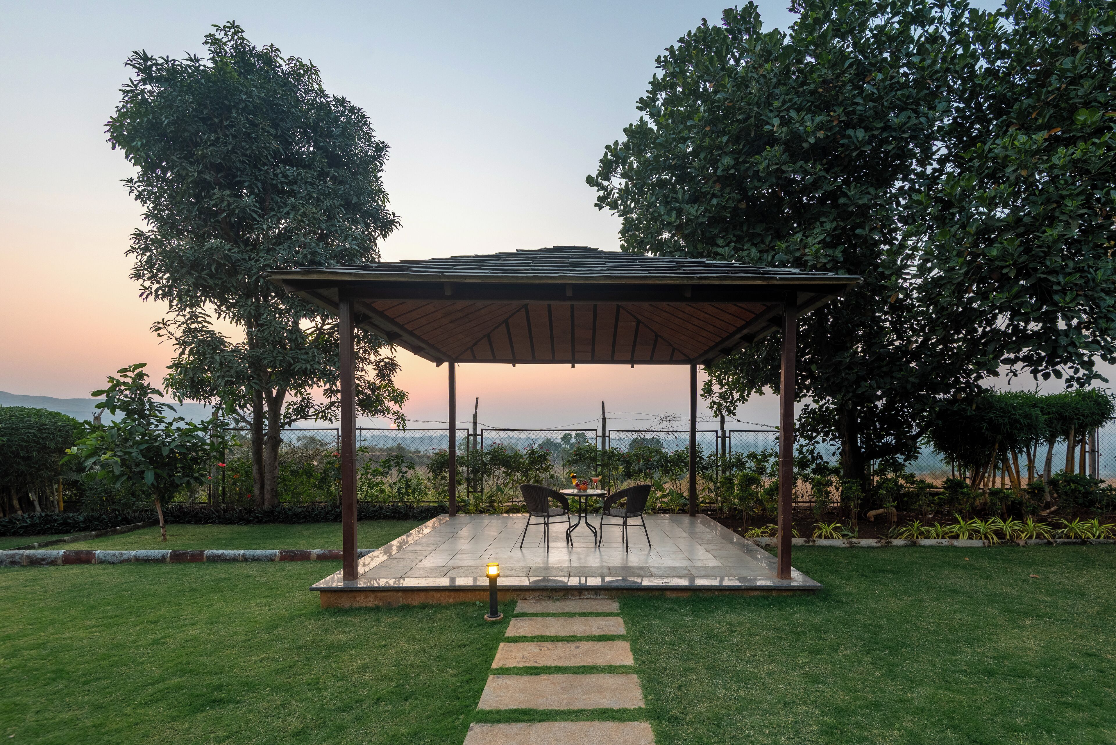 A gazebo with a table and chairs, surrounded by a well-maintained lawn and trees, overlooking a scenic view.